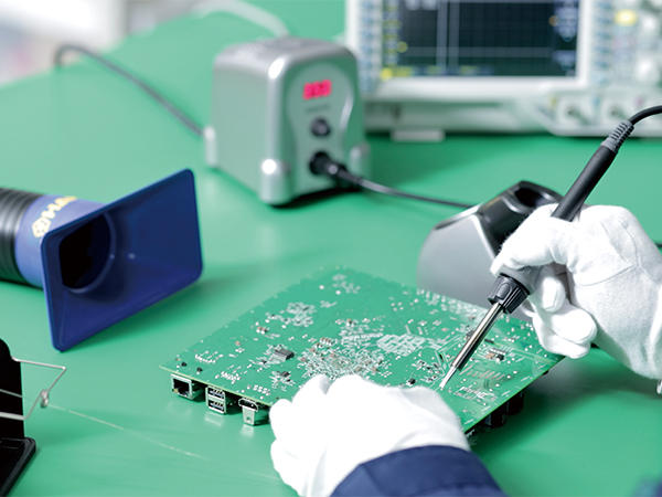 Person soldering on green circuit board with Hakko FX-888DX soldering station in background