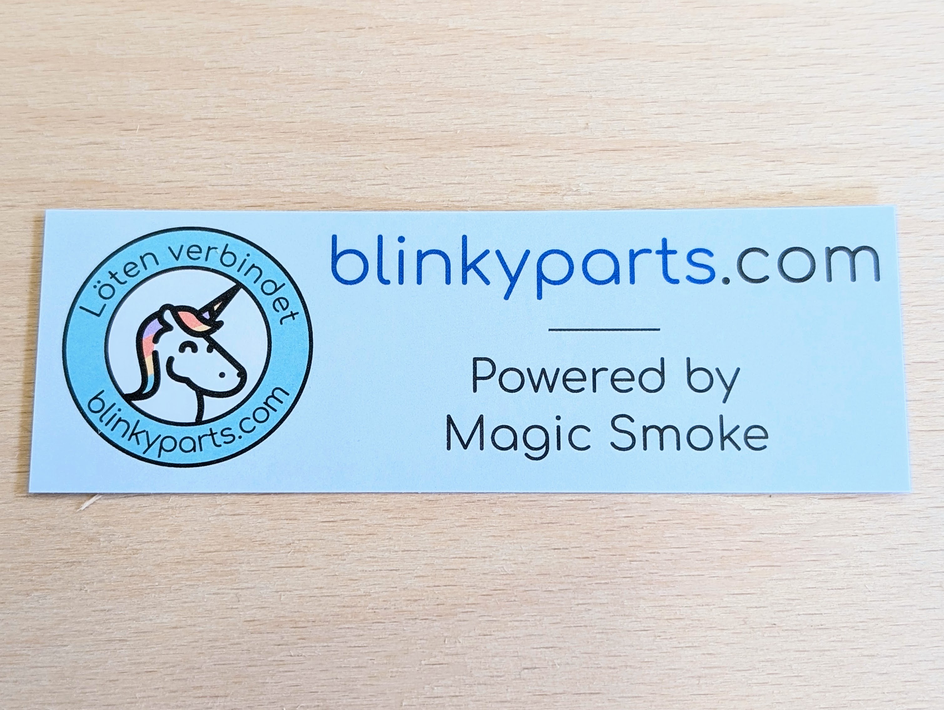 A single sticker, not affixed Blinkyparts logo sticker, single view – electronics branding Alt text: Single Blinkyparts logo sticker, not affixed, showing detailed company logo with web address and ‘Powered by magic smoke’ lettering