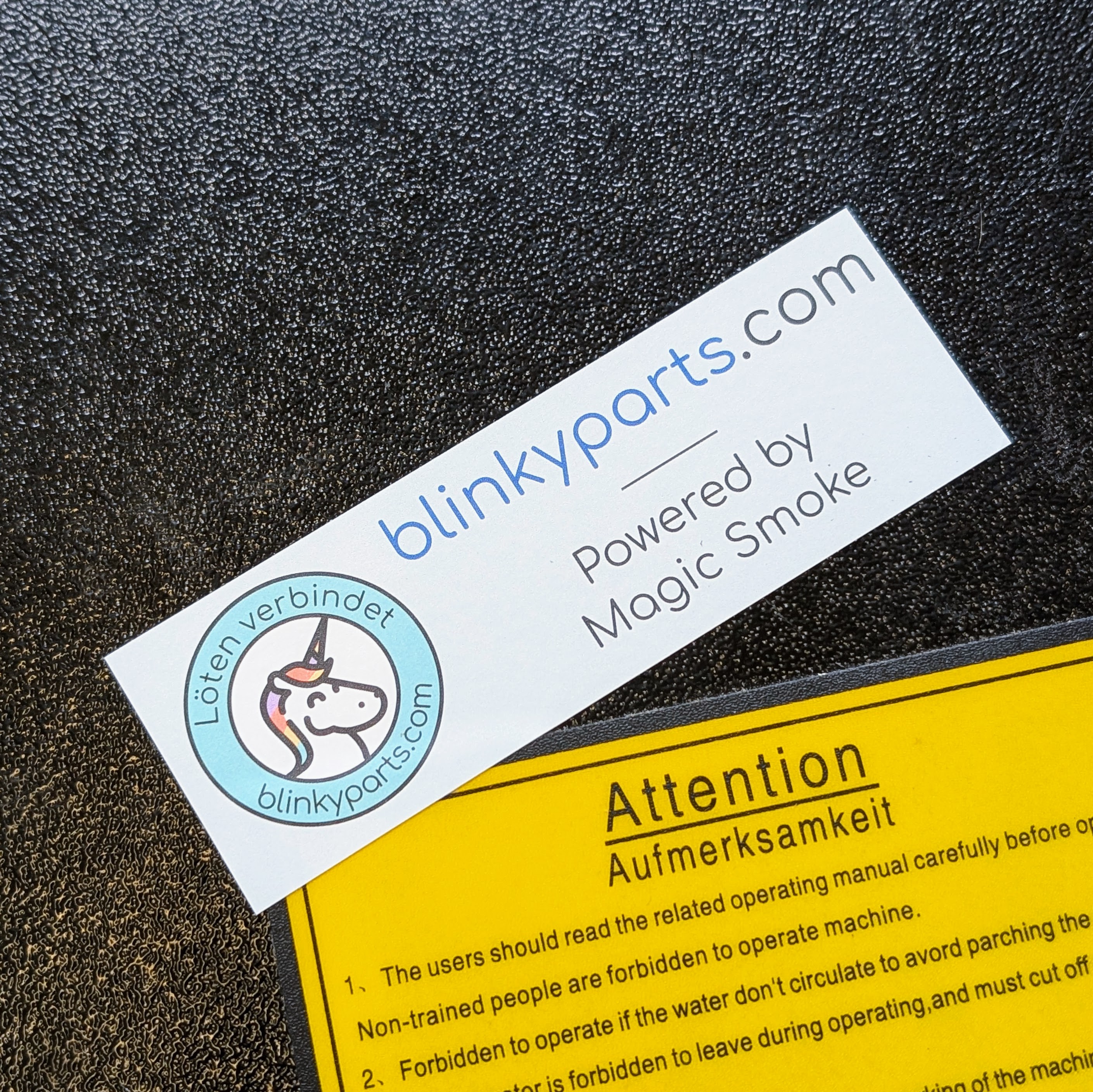 Blinkyparts logo sticker on laser cutter - Maker equipment branding Blinkyparts logo sticker affixed to laser cutter, showing practical application of company logo on maker equipment with ‘Powered by magic smoke’ lettering