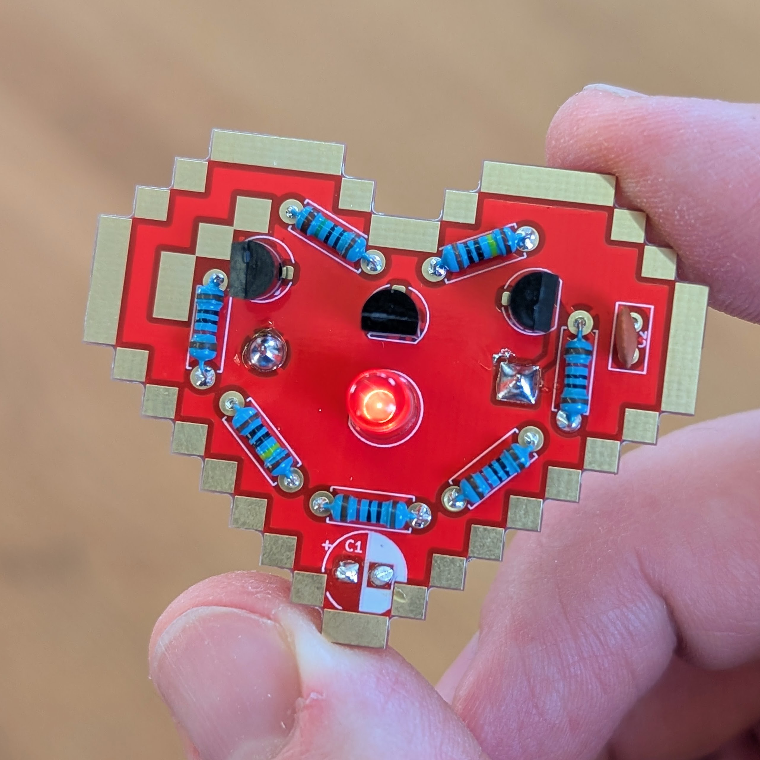 Heartbeat Lötbausatz fertig aufgebaut: Herzförmige Platine mit pulsierender LED in der Hand – fertiges Projekt